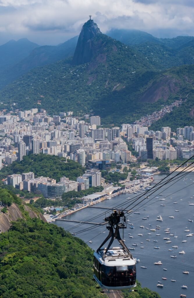 a cable car going up a mountain with a city in the background - Rio de Janeiro
