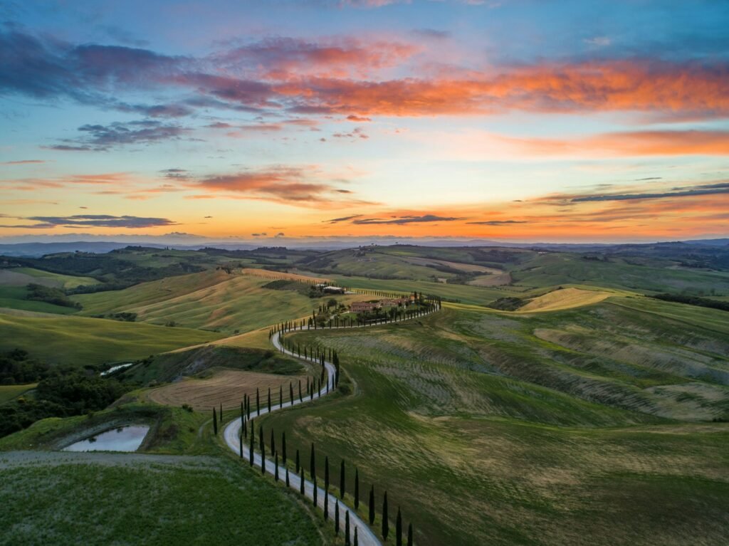 Toscana - road between green grass field near mountains under blue and brown sky at golden hour